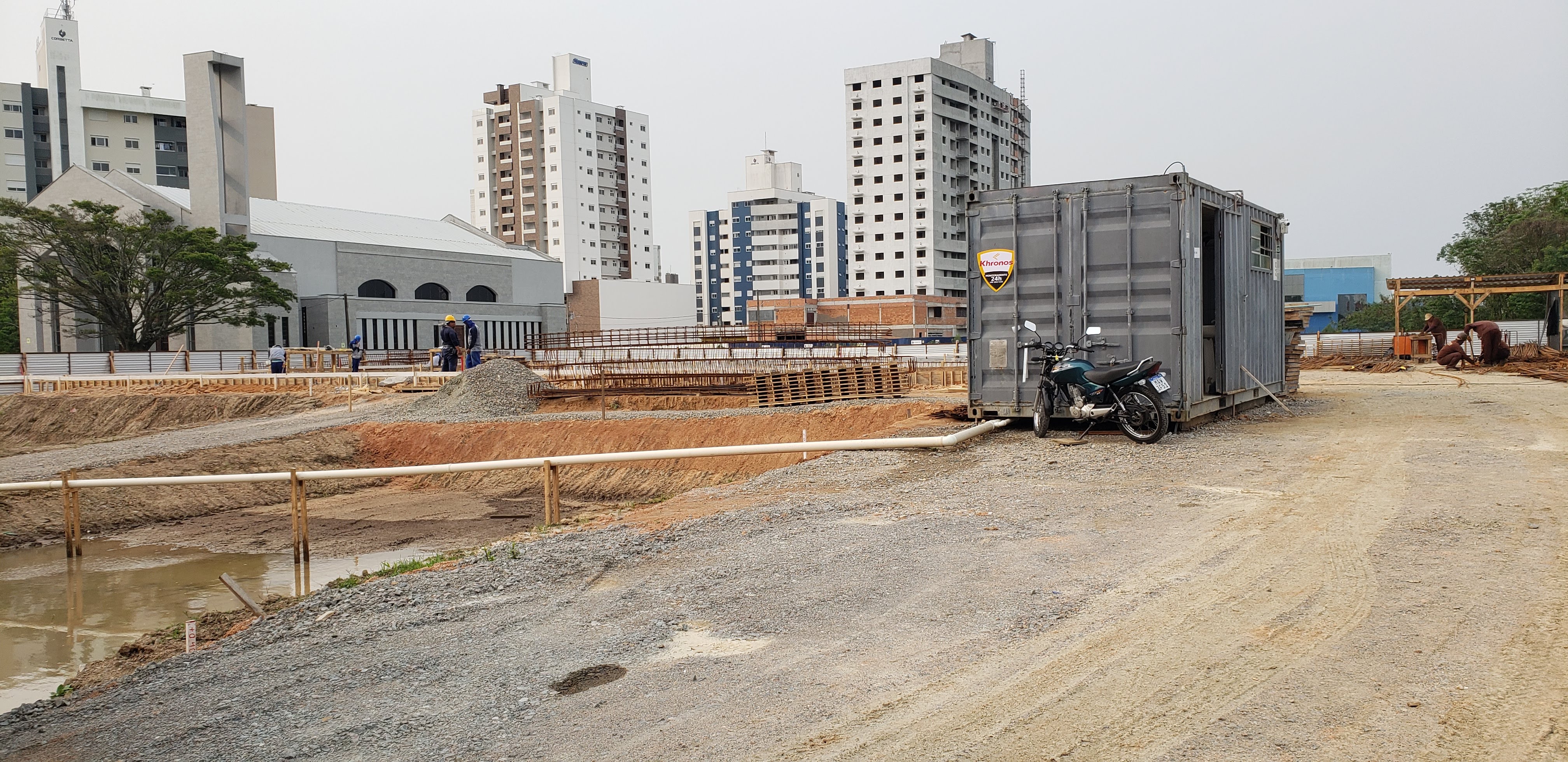 Foto - obra mostrando terreno, armaduras, um conteiner de instalações provisórias e alguns trabalhadores