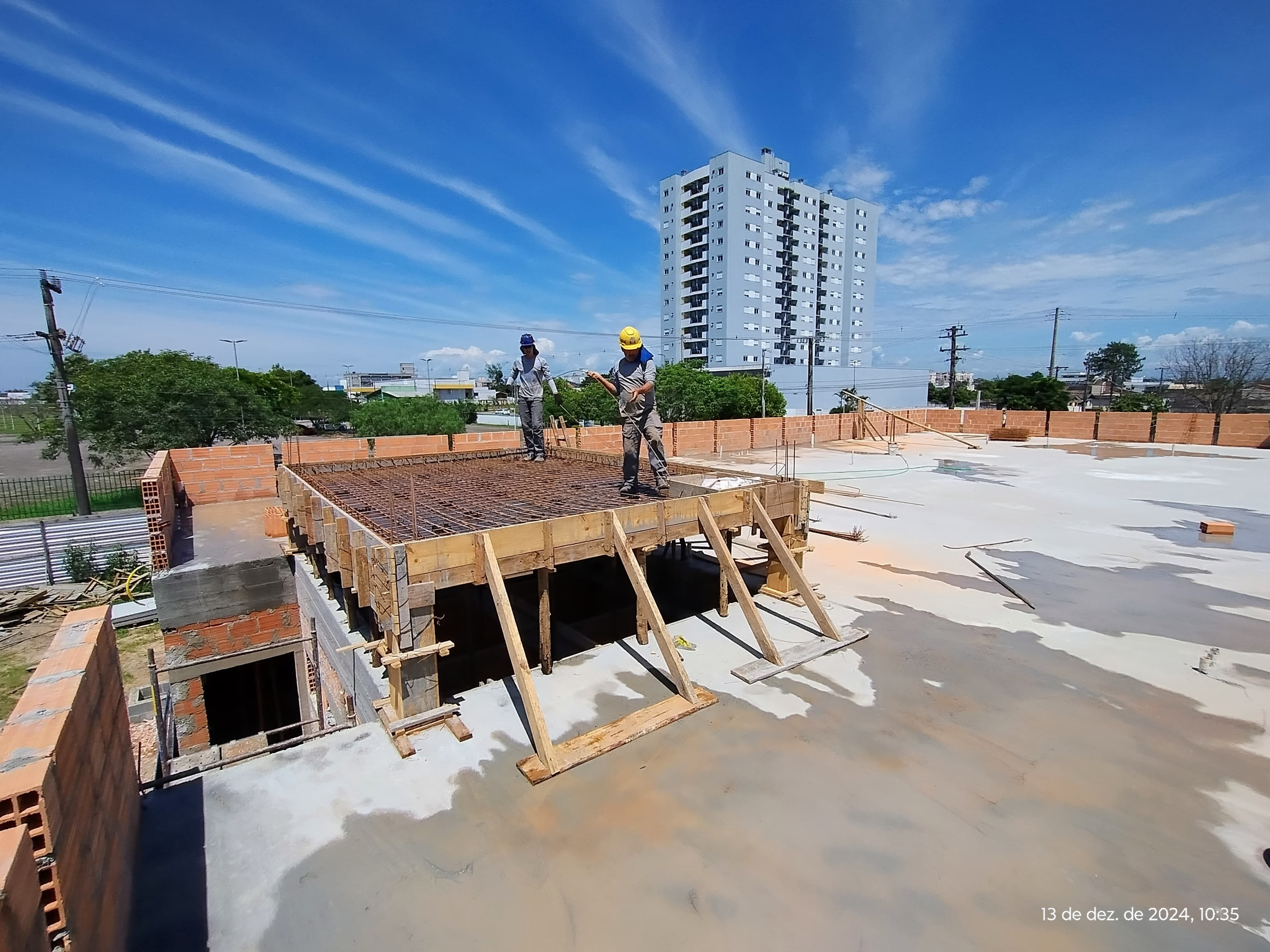 Vista da laje de cobertura do prédio após concretagem com 2 operários trabalhando 