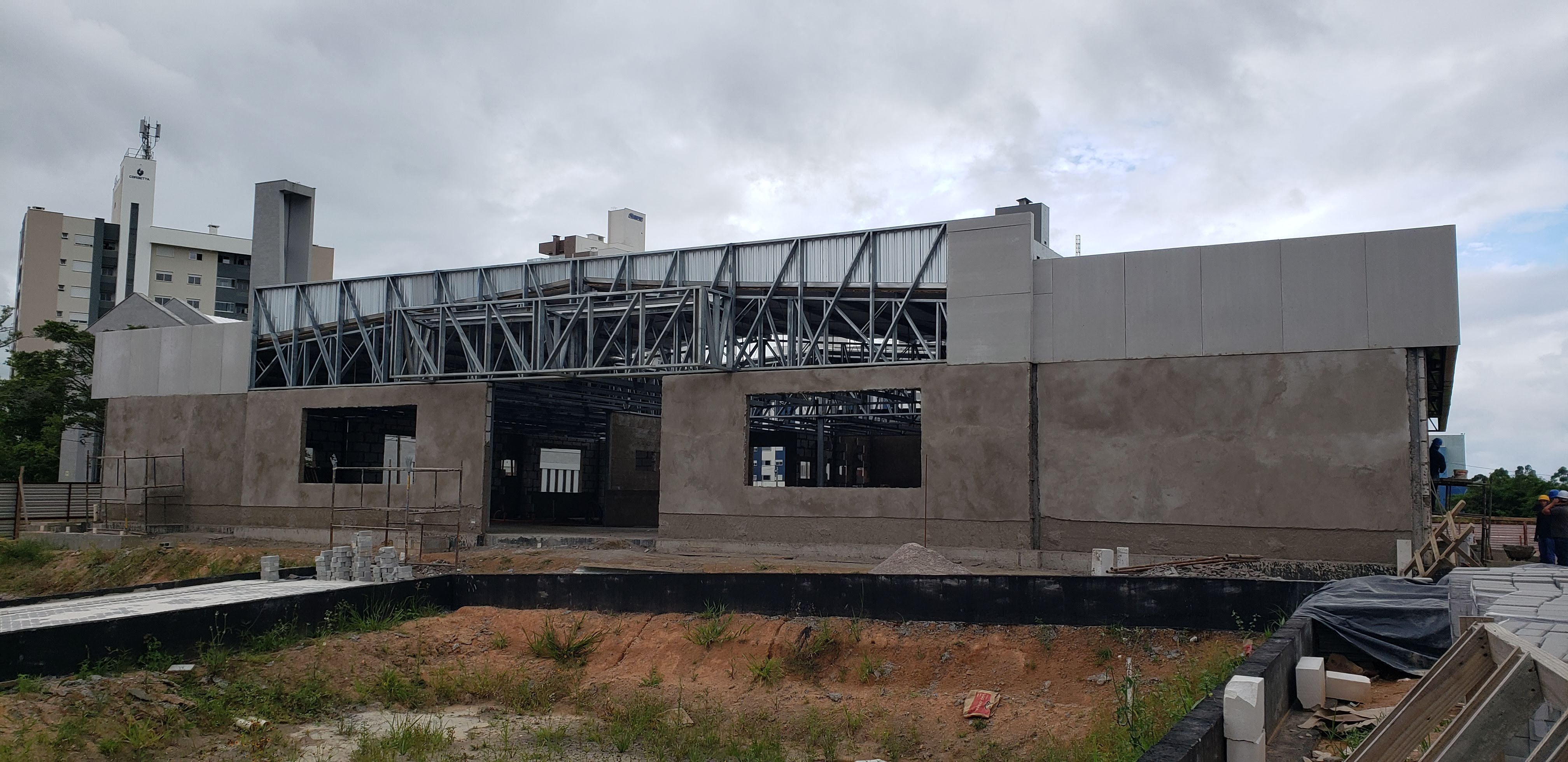 foto - Vista geral da fachada frontal da obra com reboco, estrutura métalica do telhado, calçada executados