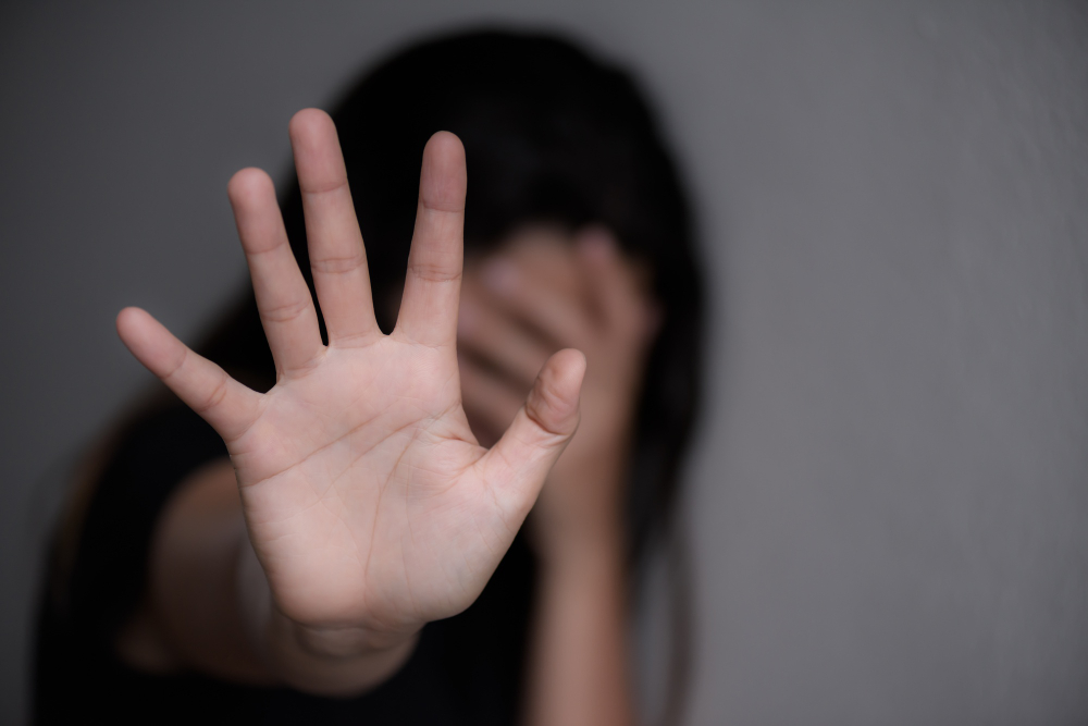 Foto de uma mulher de cabeça baixa e com palma de uma das mãos apontando para a câmera