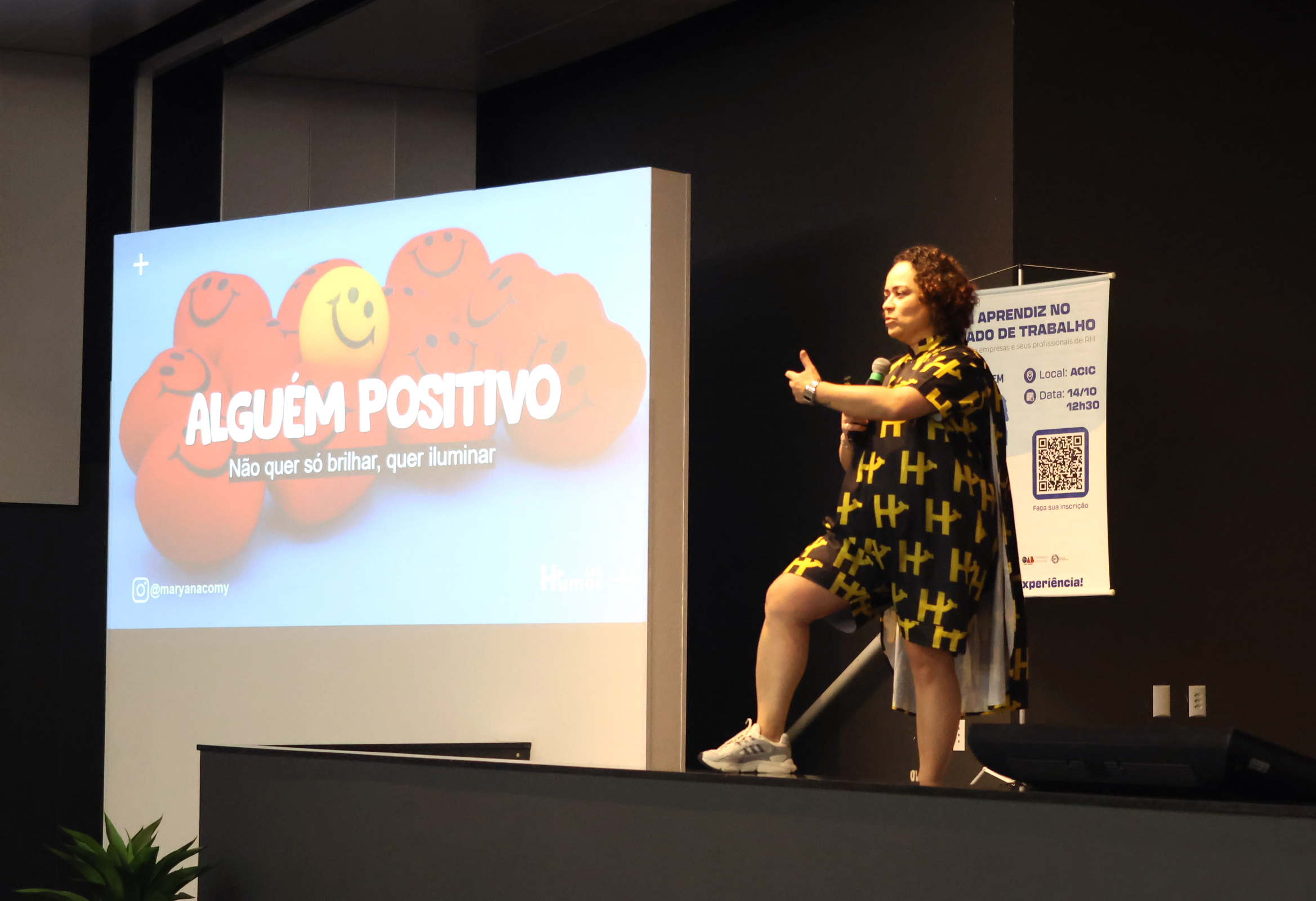 Palestrante fala em auditório durante apresentação com o tema “Alguém positivo: não quer só brilhar, quer iluminar”.