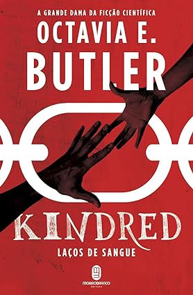 Para todos verem: Capa do livro vermelha, com duas mãos se encostando dentro de uma corrente branca, onde se lê: "A grande dama da ficção científica. Octavia E. Butler. Kindred: laços de sangue. Morro Branco Editora".