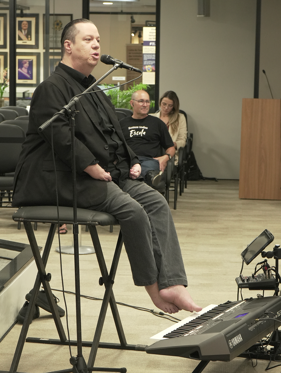 Músico sentado em uma banqueta alta descalço. Abaixo dos pés, um teclado.