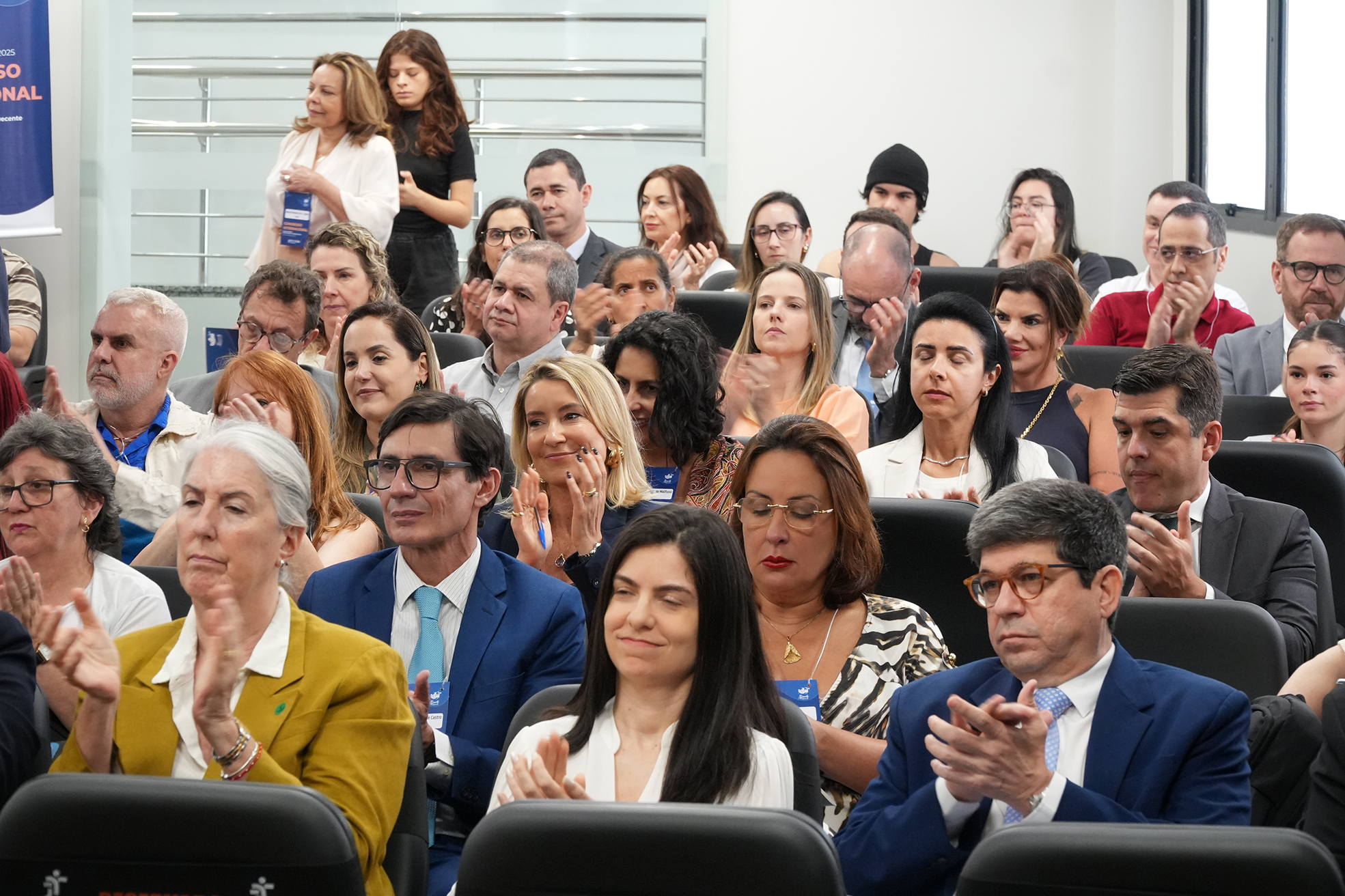 Foto de um público composto de homens e mulheres aplaudindo uma palestra em uma sala de auditório