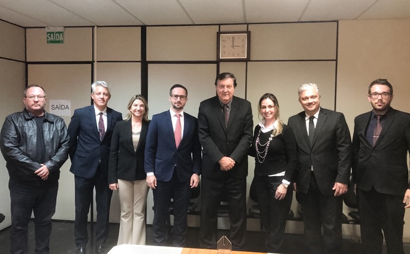 Seis homens e duas mulheres estão lado a lado, posando e sorrindo para a foto em uma sala de reunião