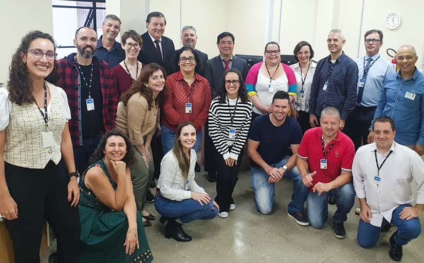 Um grupo de pessoas, entre elas homens e mulheres, posam para a foto em uma sala de escritório