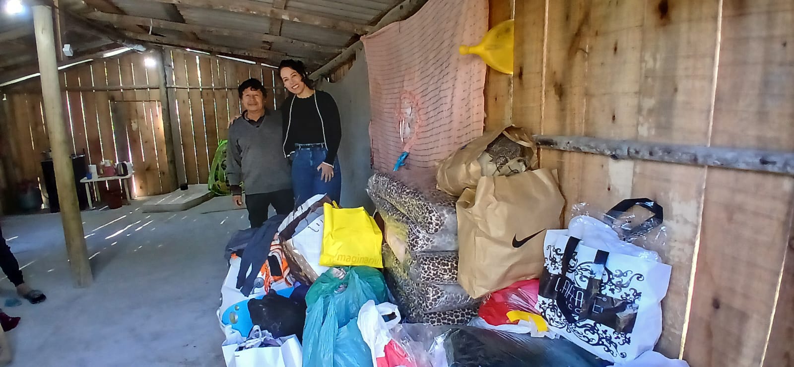 Um senhor indígena e uma mulher abraçados ao lado de sacolas de doações