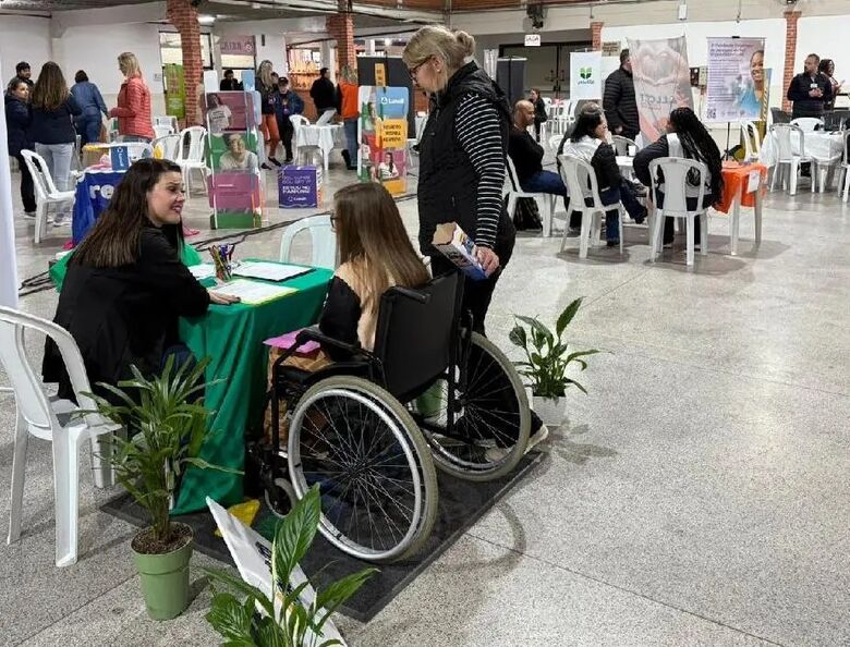 Foto de um evento acontecendo. No primeiro plano uma mulher na cadeira de rodas