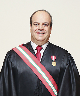 Um homem de cabelos castanhos, vestindo uma toga e uma faixa está sorrindo para a foto