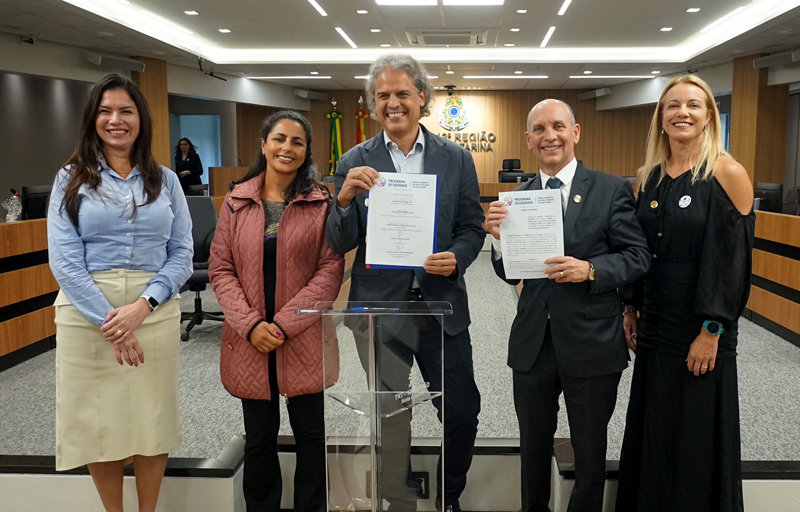 Cinco pessoas posando para foto segurando termo de adesão.