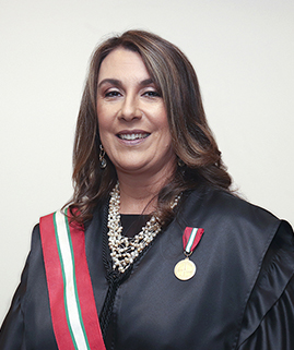 Uma mulher de cabelos castanhos, vestindo uma toga e uma faixa está sorrindo para a foto