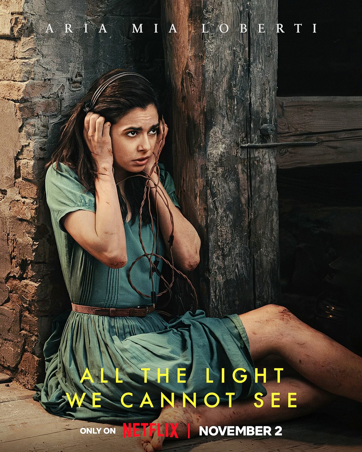 Para todos verem: Texto: "Aria Mia Loberti. All The Light We Cannot See. Only on Netflix. November 2 ". Ilustração: Banner em que há uma mulher machucada que está sentada e utilizando fones no ouvido.