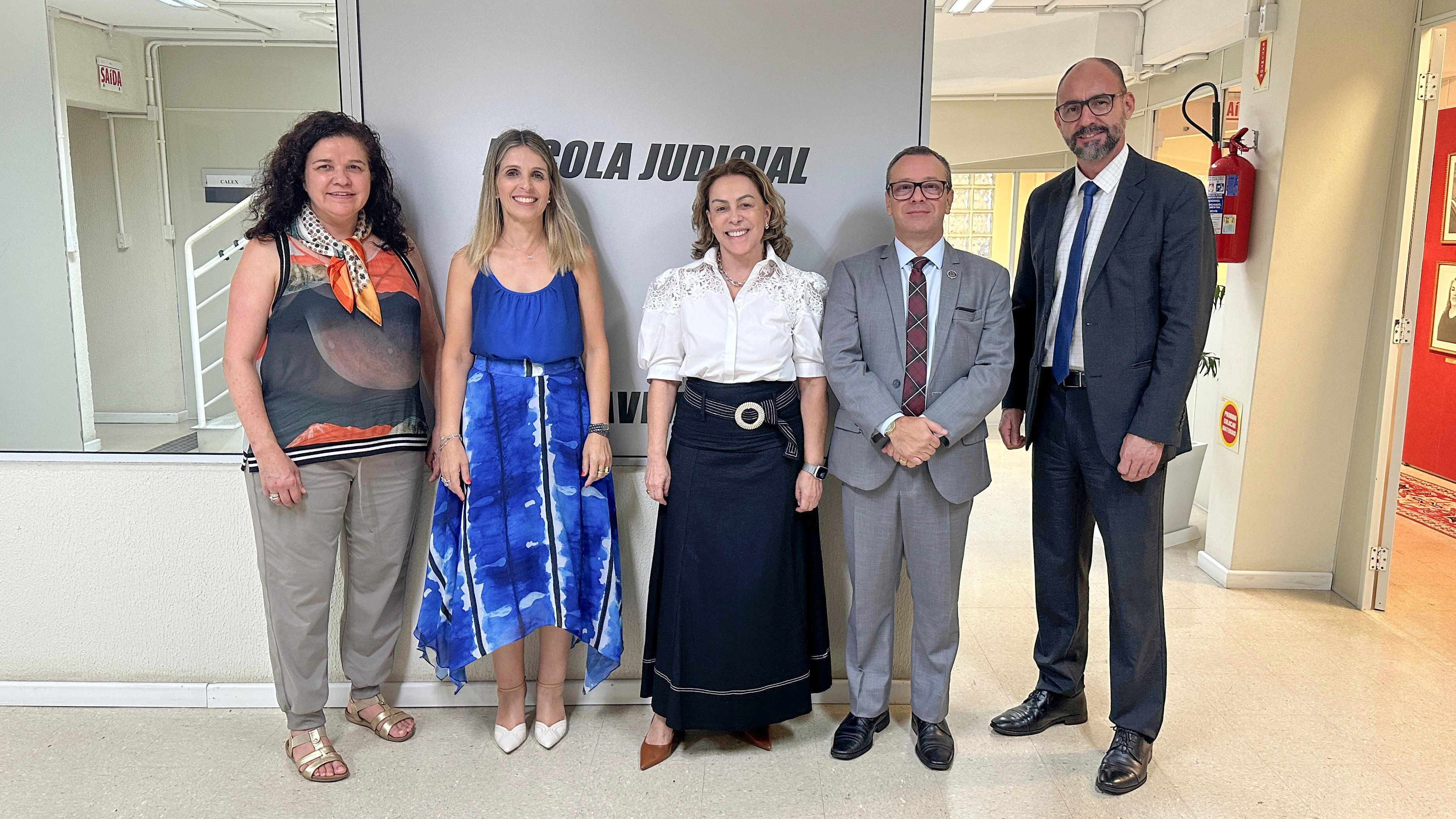 Cinco pessoas posam para foto em frente a um painel onde se lê "Escola Judicial". São três mulheres e dois homens. Ao centro, a ministra do TST, Dora Maria da Costa.