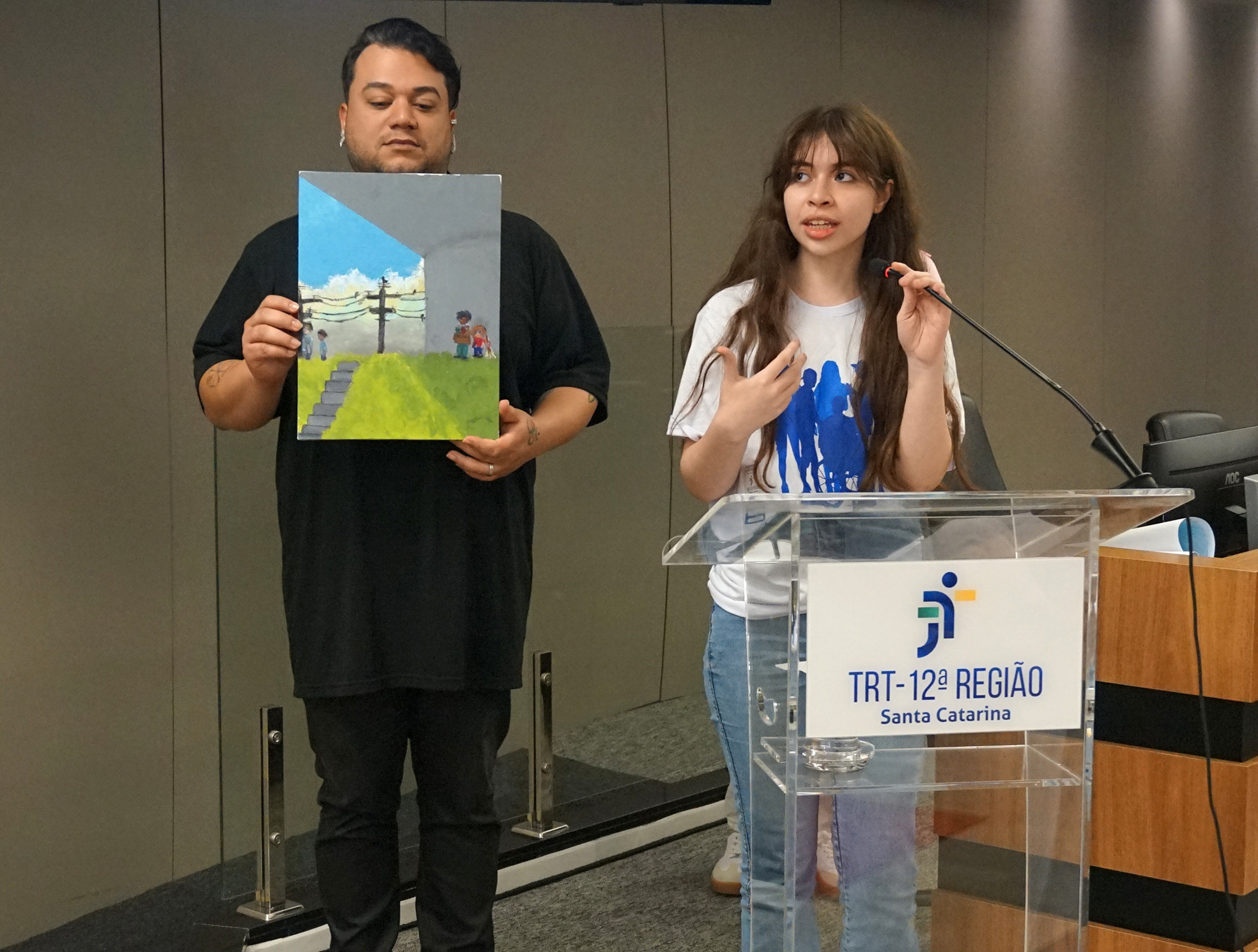 Estudante apresenta seu trabalho: uma pintura em tela mostrando duas crianças embaixo de um viaduto.