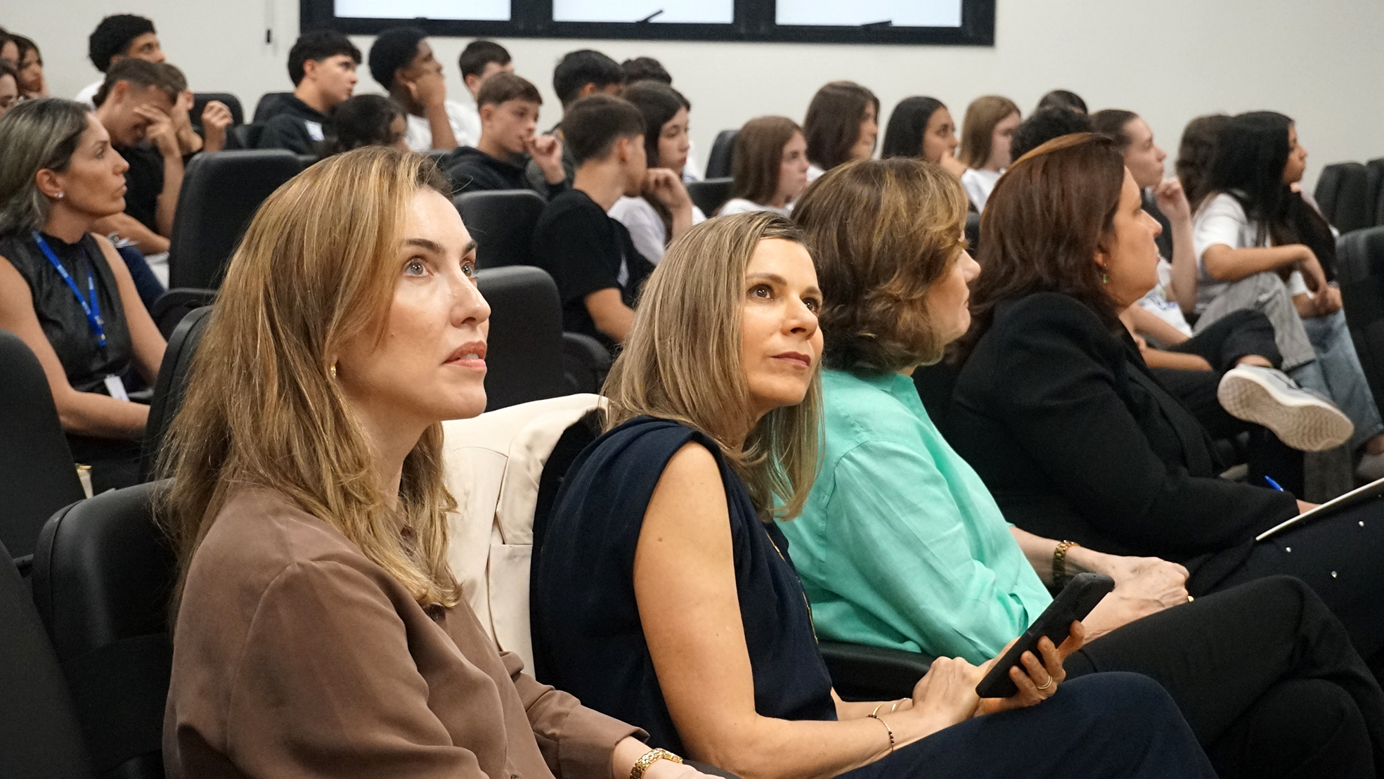 Duas mulheres loiras bem vestidas olham para cima, provavelmente para um telão