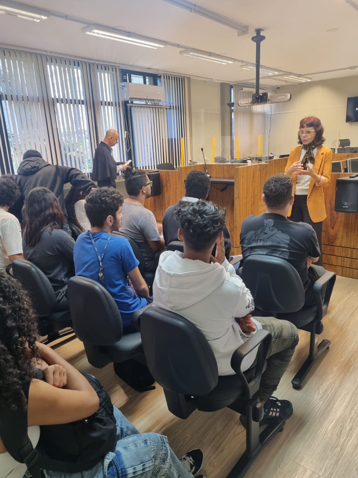 grupo de pessoas sentadas assistindo uma mulher de roupa amarela