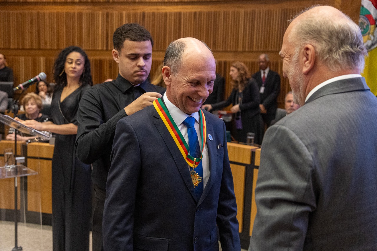 Imagem de um homem sorrindo, aguardando enquanto outro homem coloca nele a medalha de honra