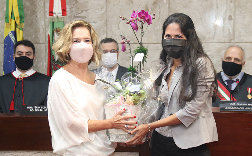 Servidora aposentada Marilde Mafra e servidora Renata Freitas posam para foto segurando uma orquídea rosa.
