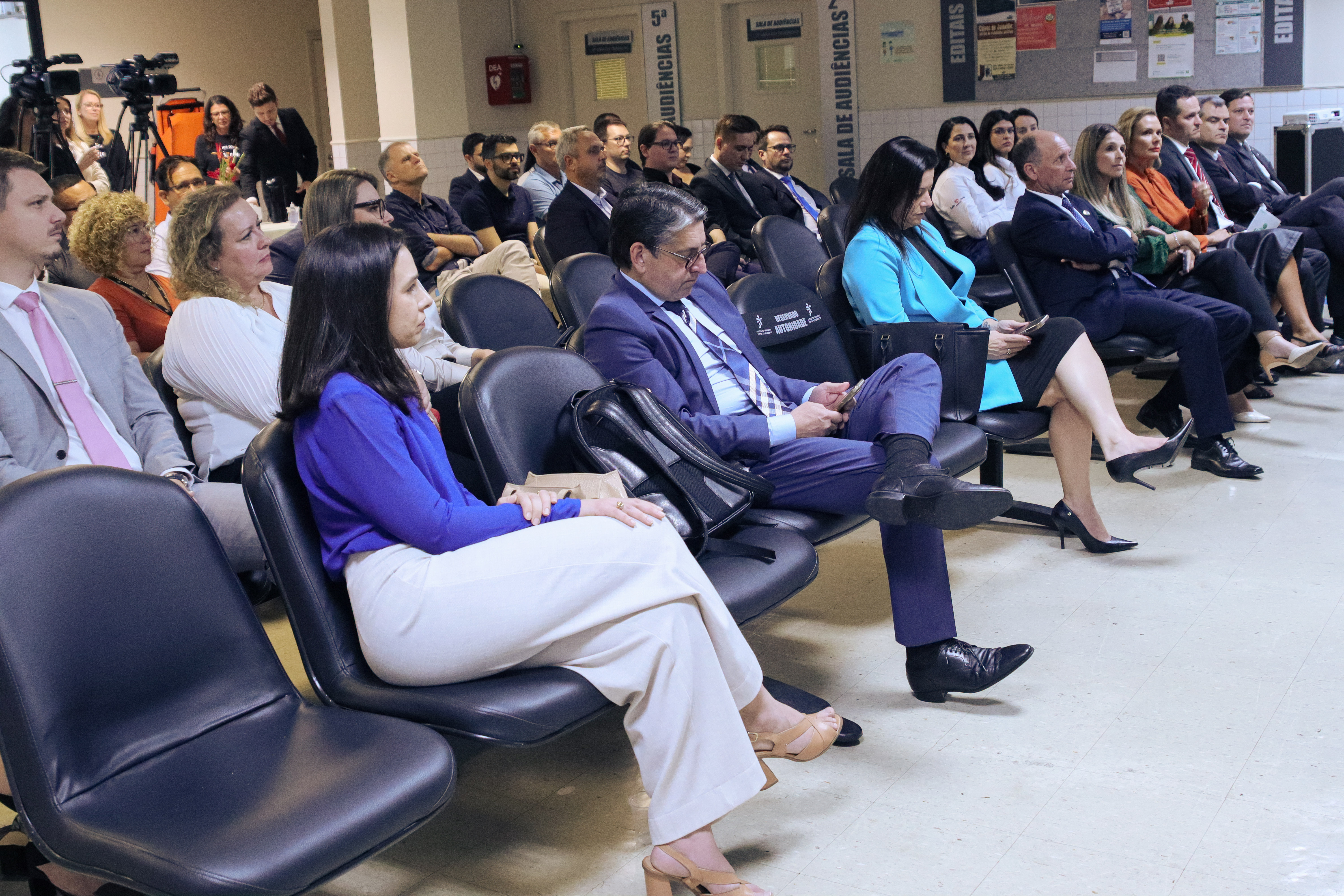 Grupo de 30 pessoas sentadas, num auditório, acompanham atentamente uma palestra 