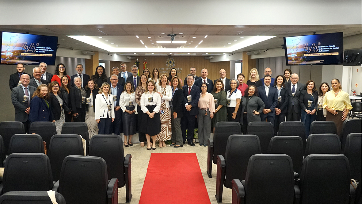 Grupo de participantes posa para foto oficial em auditório, alinhados em frente ao púlpito do evento.