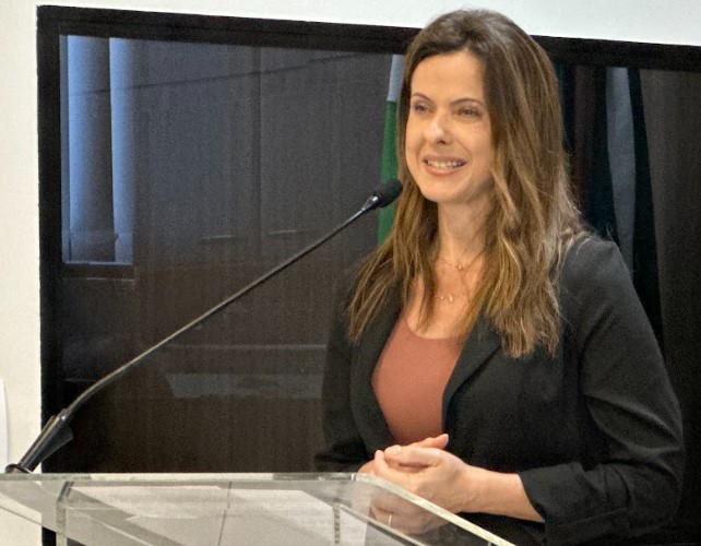 Mulher branca, cabelo castanho fala ao microfone 