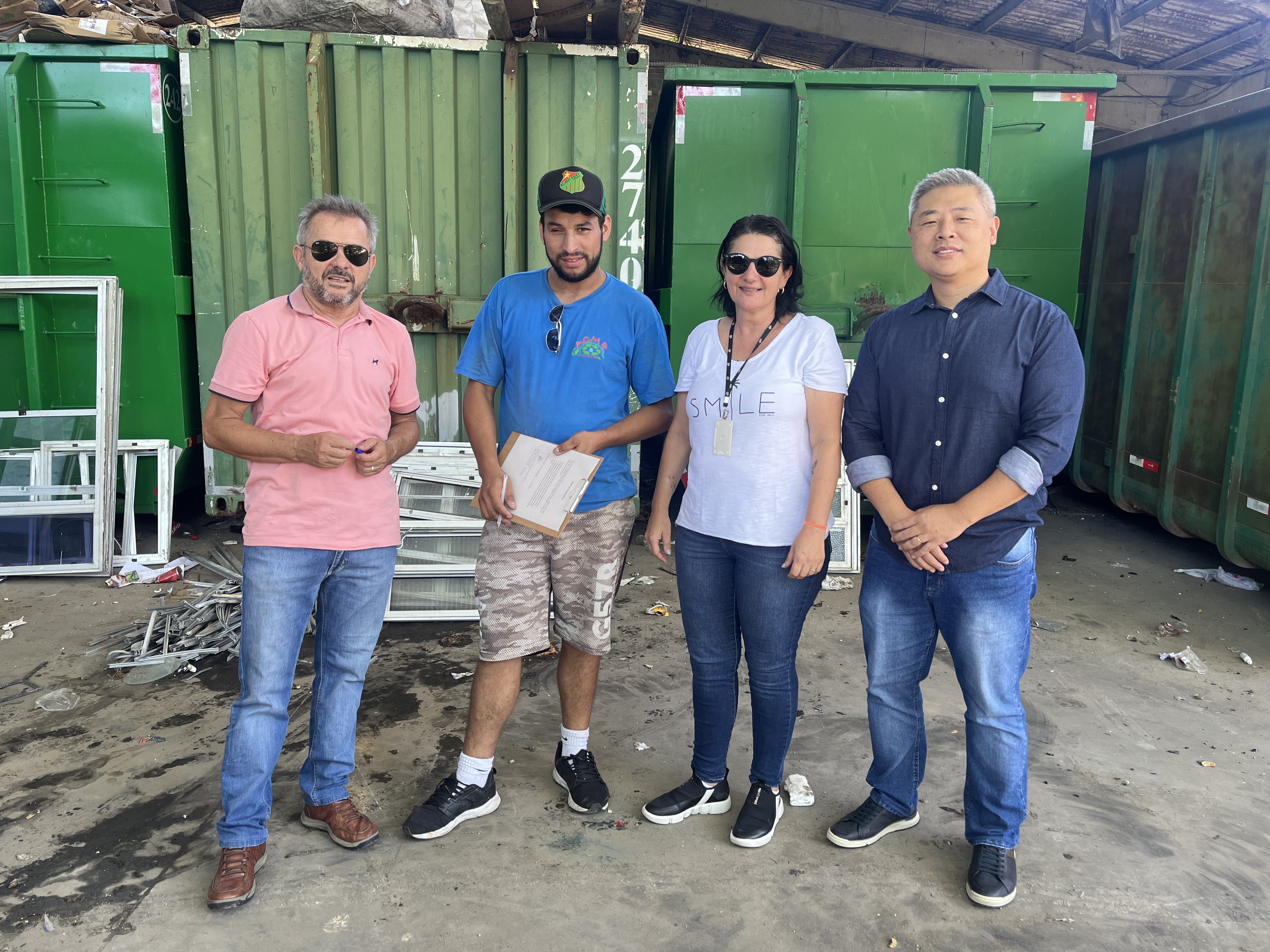 Três homens e uma mulher posam para foto, na frente de alguns entulhos