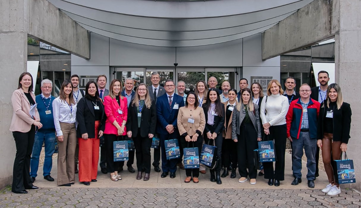 Grupo de cerca de 30 pessoas posa para a foto em frente à entrada de uma empresa