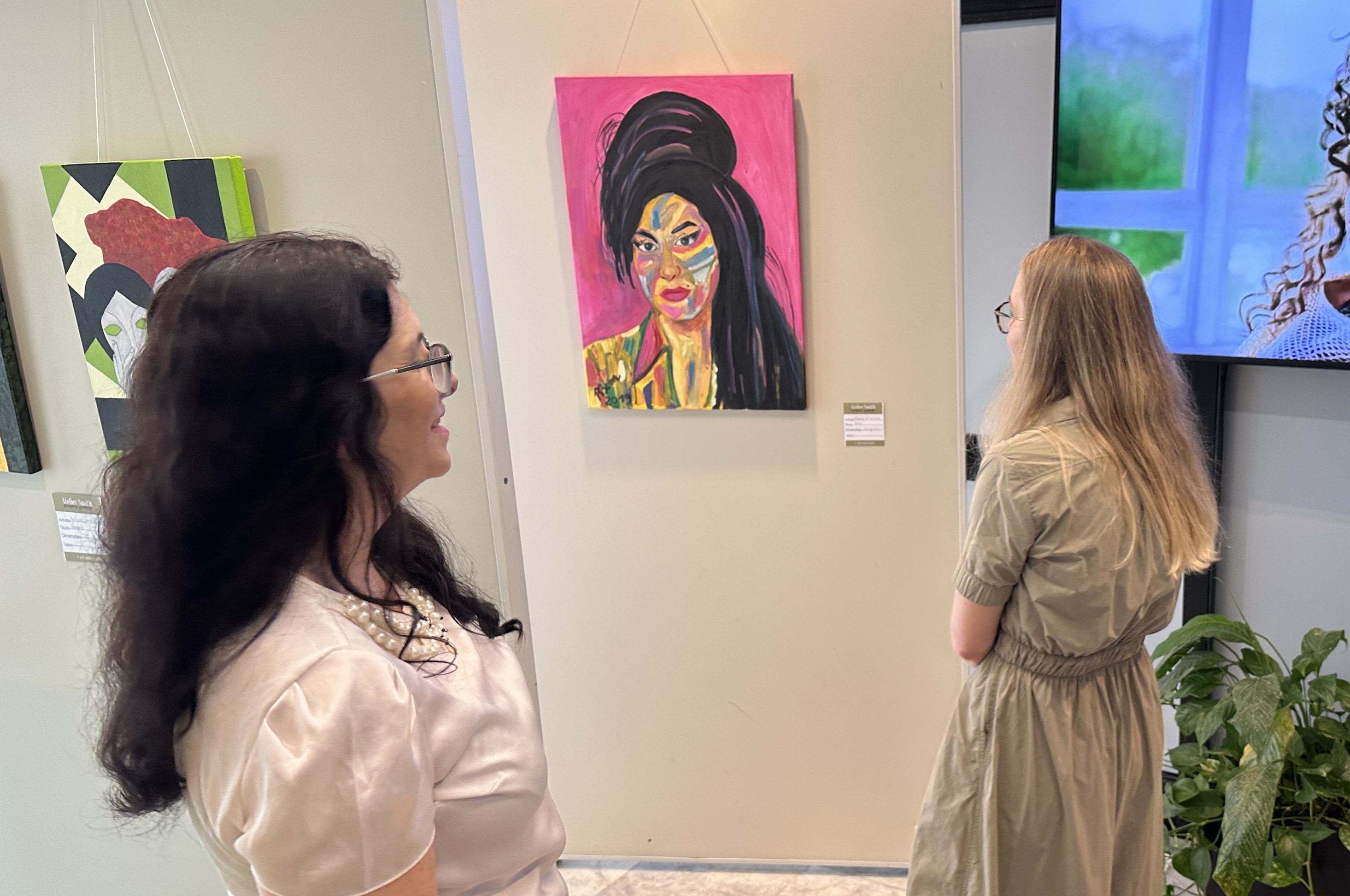 Três mulheres observam um retrato estilizado de uma mulher branca de cabelos negros lisos e longos