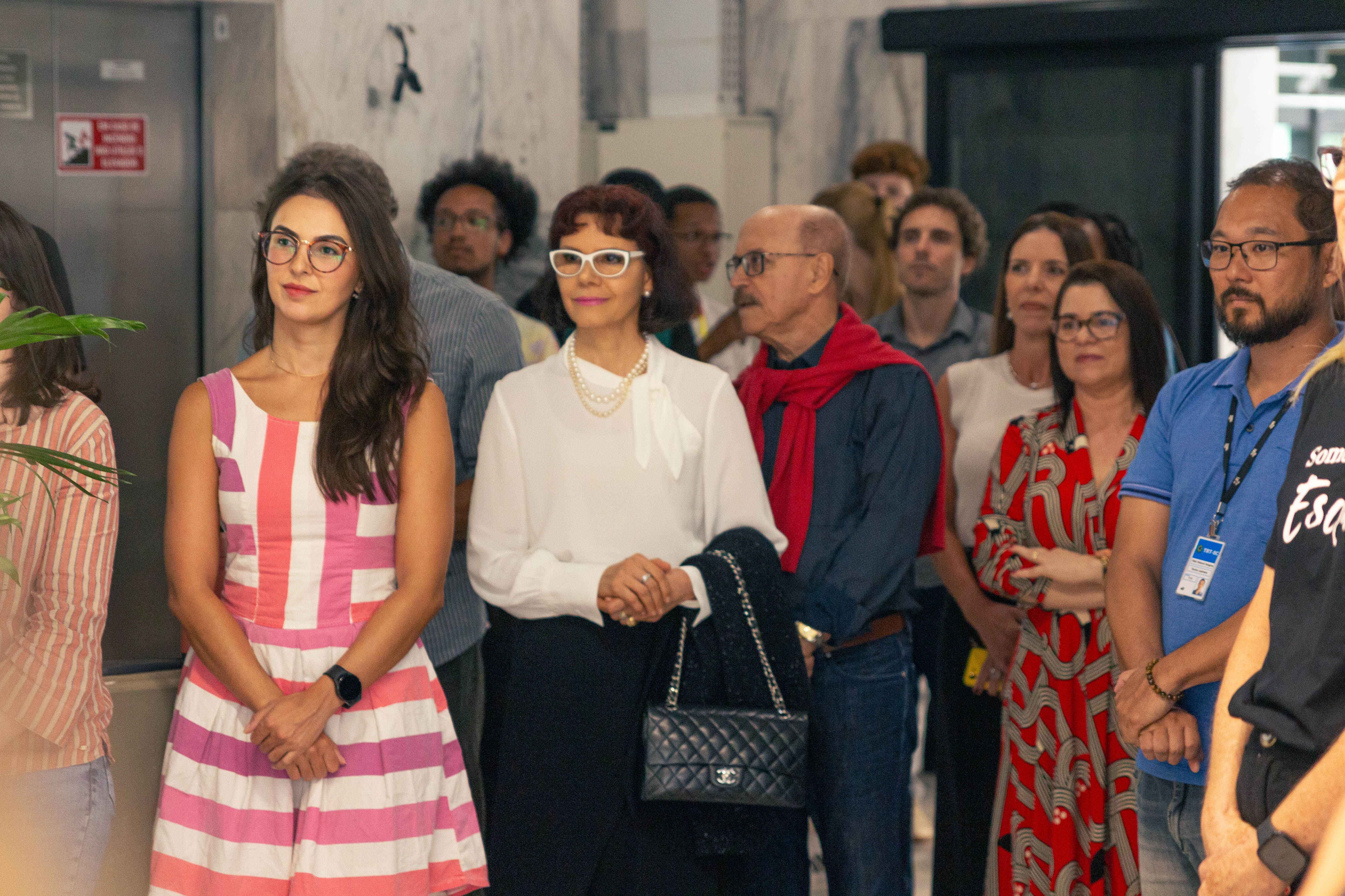 Fotografia do público do tribunal presente à abertura da exposição. As pessoas estão em pé e atentas às falas de abertura.