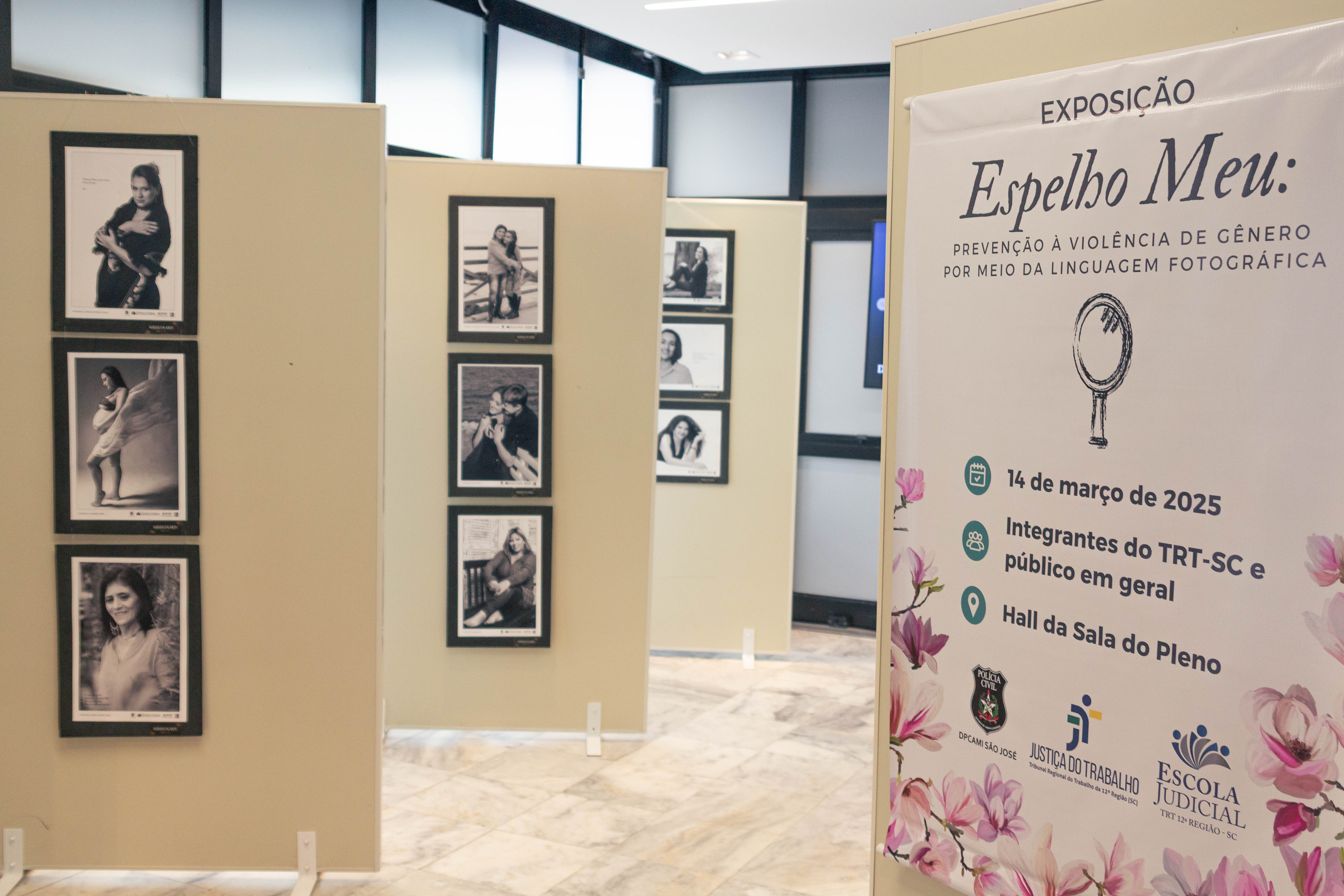 Fotografia de uma exposição fotográfica, onde é possível ver quatro painéis com fotografias tipo retrato, em preto e branco, e um painel com um banner no qual consta o nome da exposição, Espelho Meu, e os dados da abertura, como data, público-alco e local.