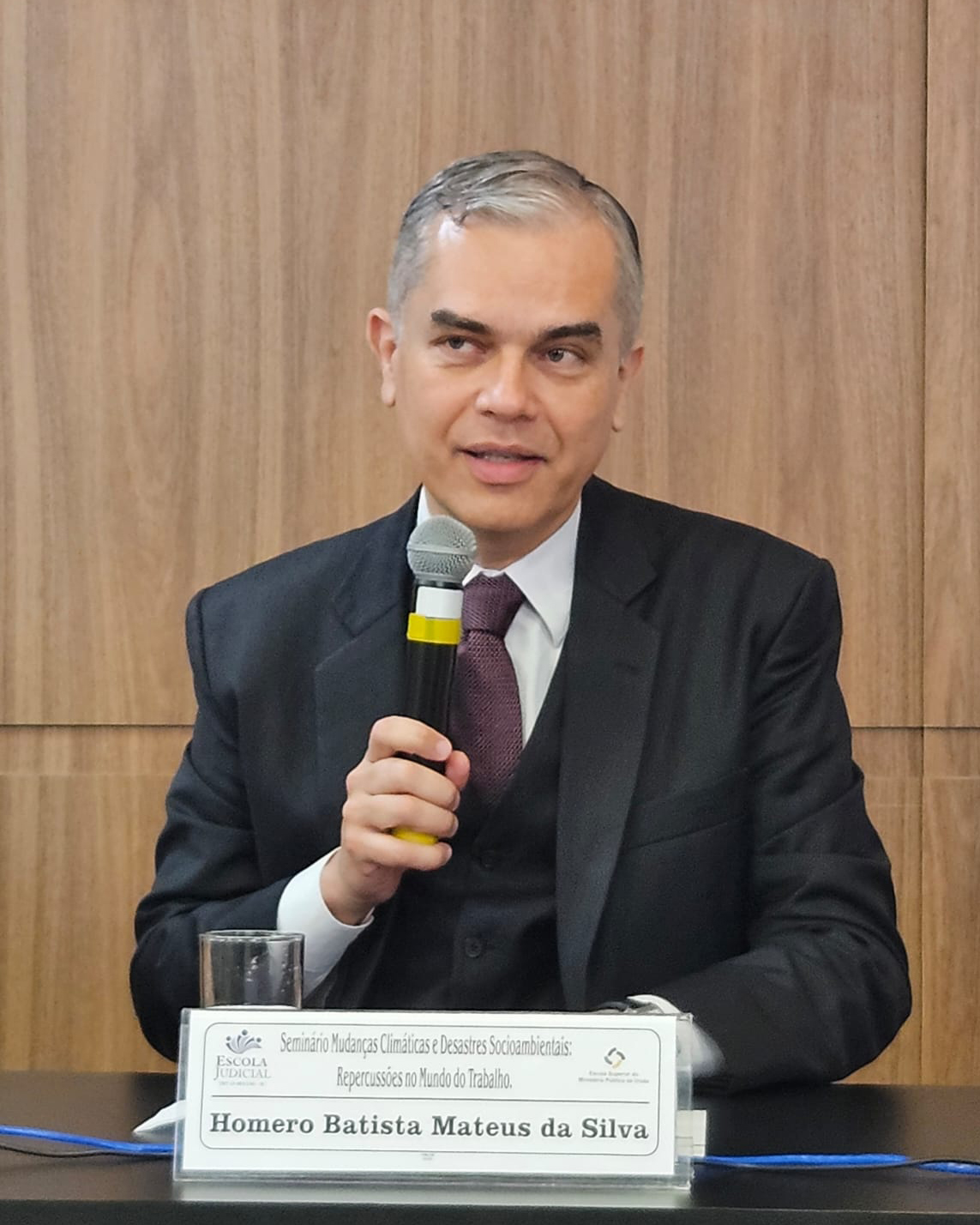 Home de terno escuro e gravata falando ao microfone