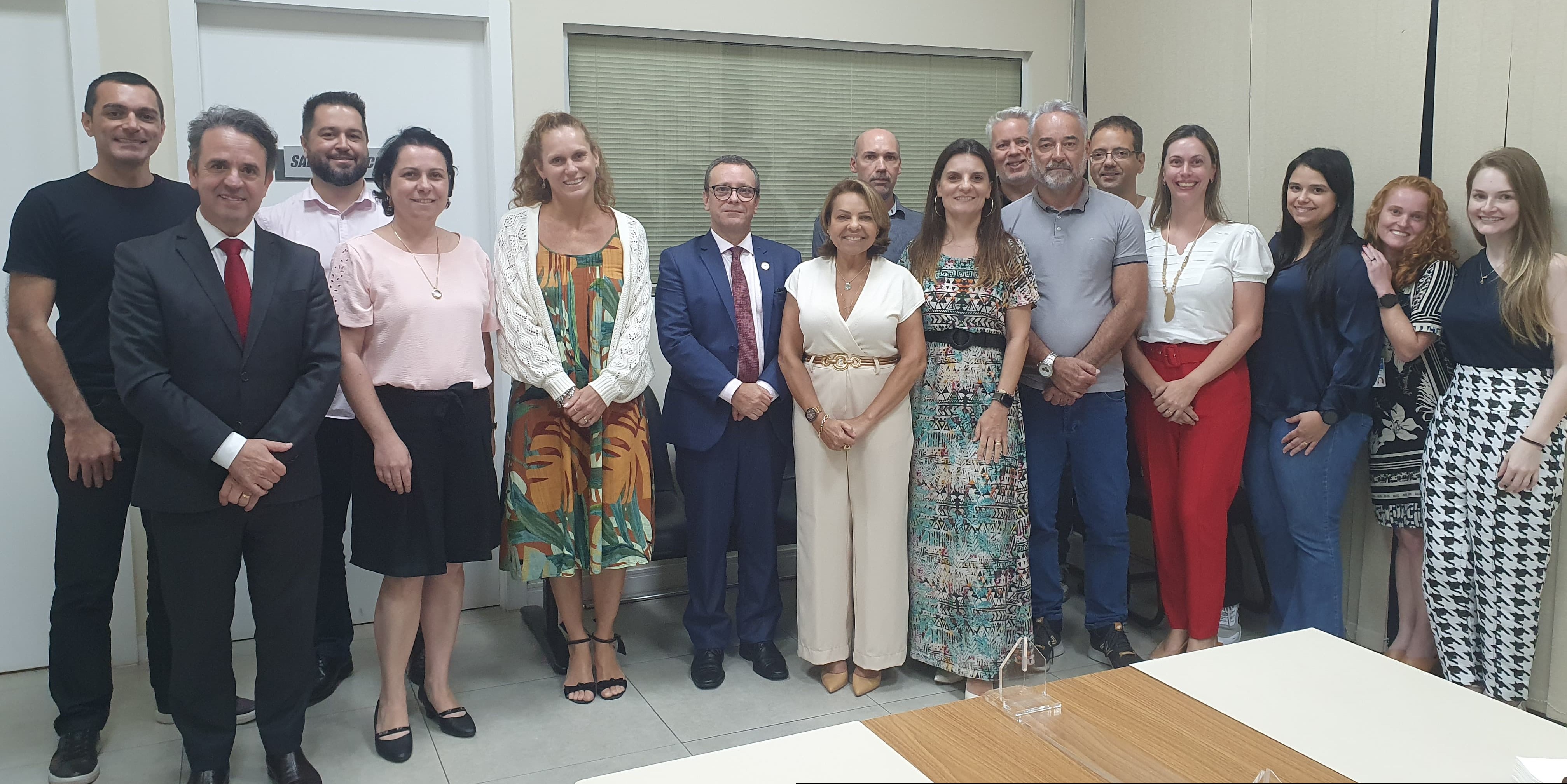 Foto de sala onde posam para foto em pé dezesseis pessoas