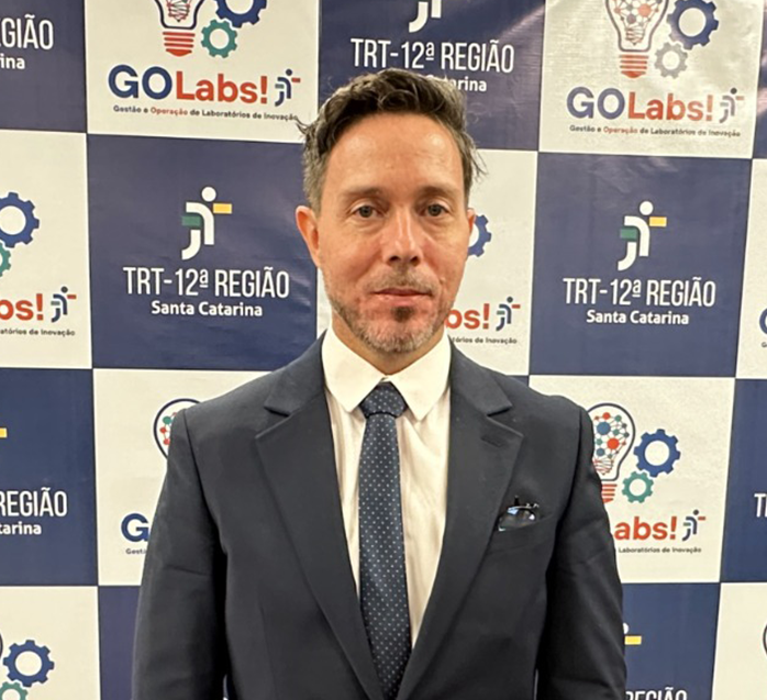 Um homem de cabelo grisalho, está em pé posando para a foto