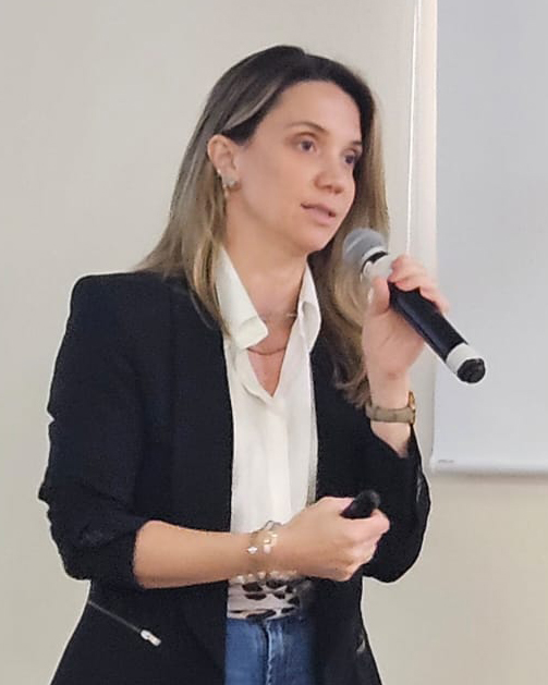 Mulher com terno escuro e camisa branca falando ao microfone