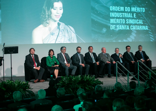 Presidente Mari Eleda sentada com outras oito autoridades no auditório da FIESC