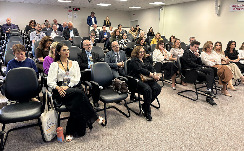 Foto de um público (homens e mulheres) assistindo uma palestra em uma sala de auditório