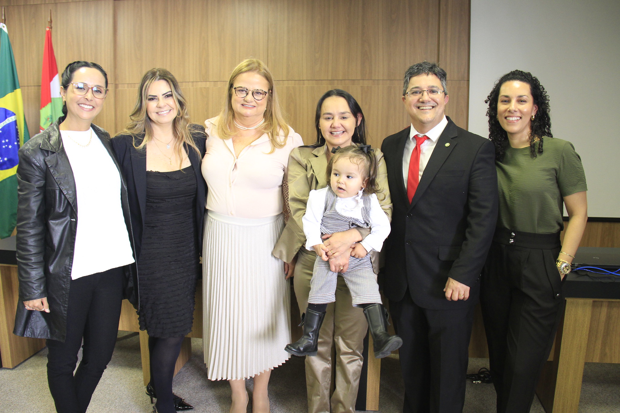 Grupo de cinco mulheres e um homem posa para a foto. Uma das mulheres segura uma menina de cerca de dois anos