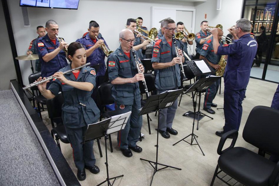 Foto de uma banda vestida com uniforme do Corpo de Bombeiros, tocando os instrumentos