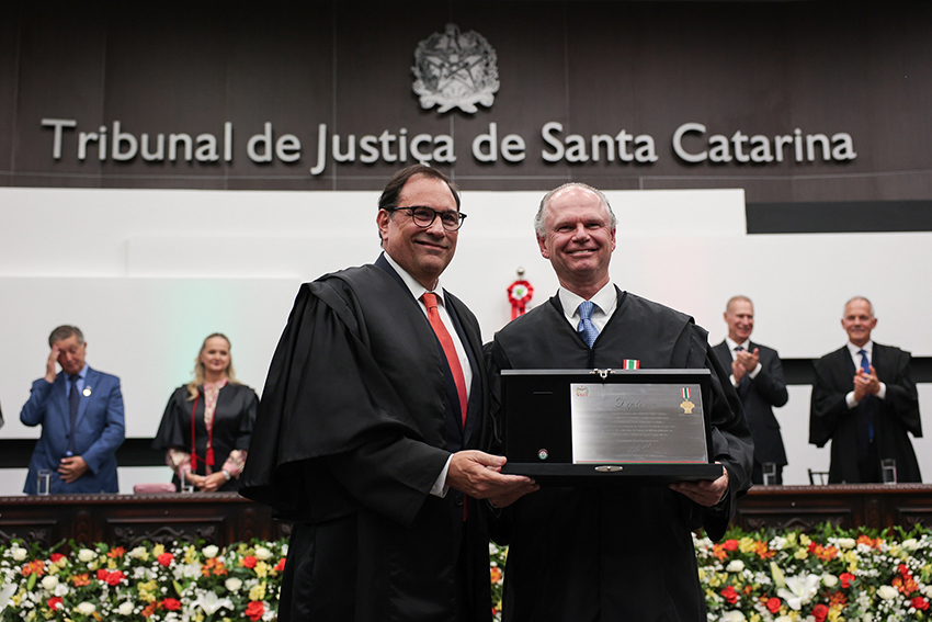 Dois homens vestindo toga e segurando placa de homenagem