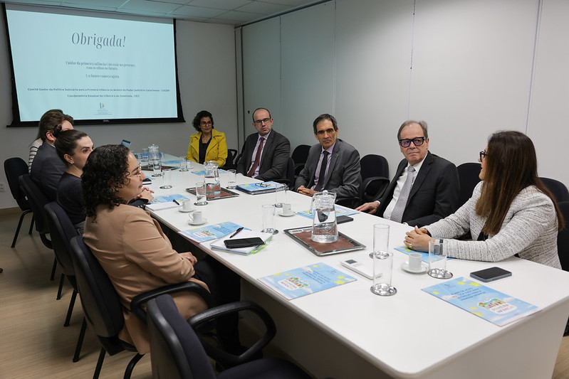 imagem de uma sala de reuniões com diversas pessoas sentadas ao redor de uma mesa.