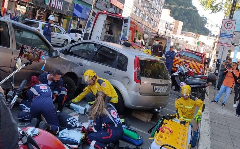 Foto de uma rua cheia de carros, pessoas e prédios. Em destaque na foto uma simulação de um resgate de acidente de trânsito.