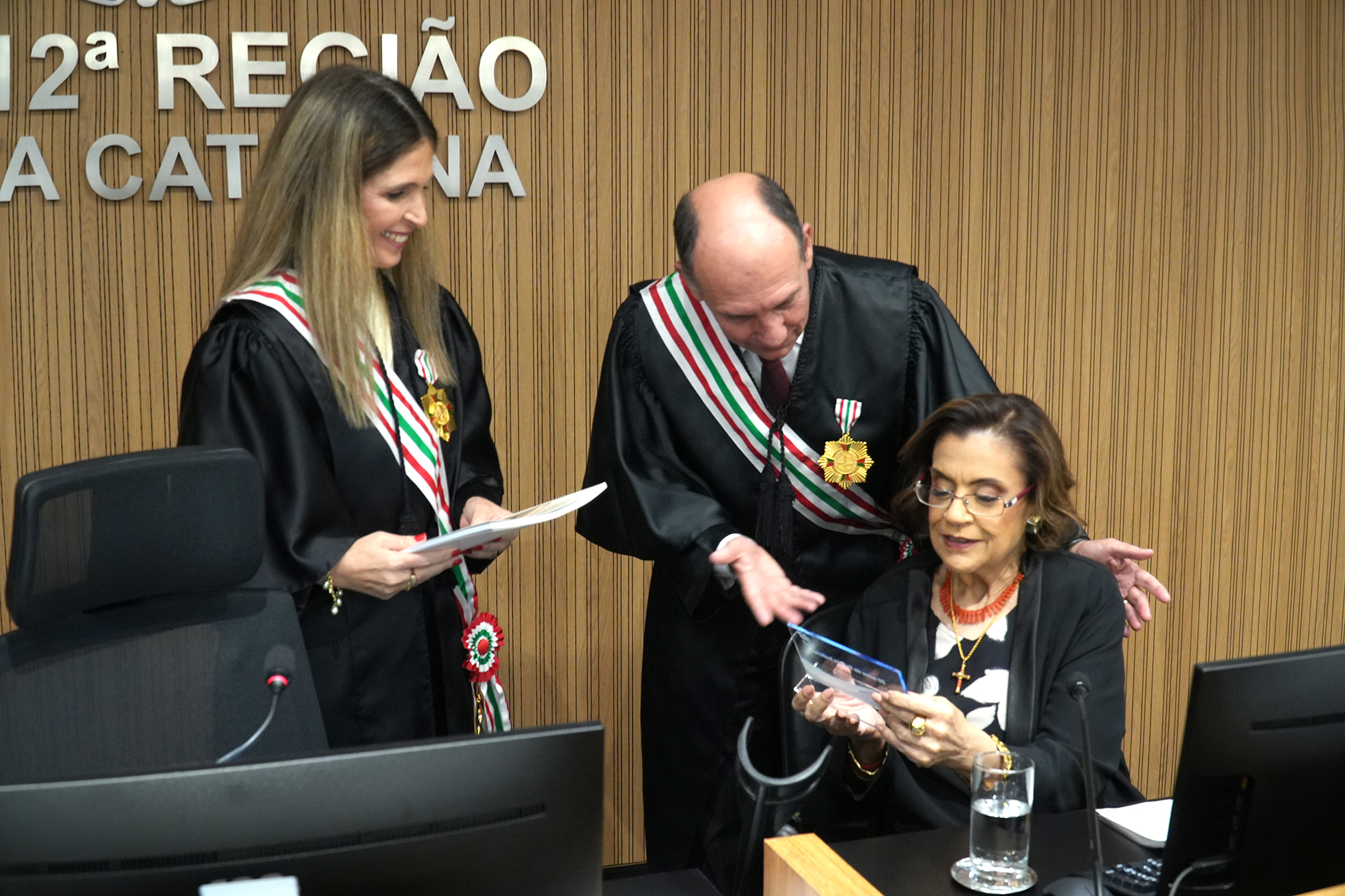 Magistrados do TRT-SC conversam sorridentes durante solenidade, com medalhas e faixas oficiais.