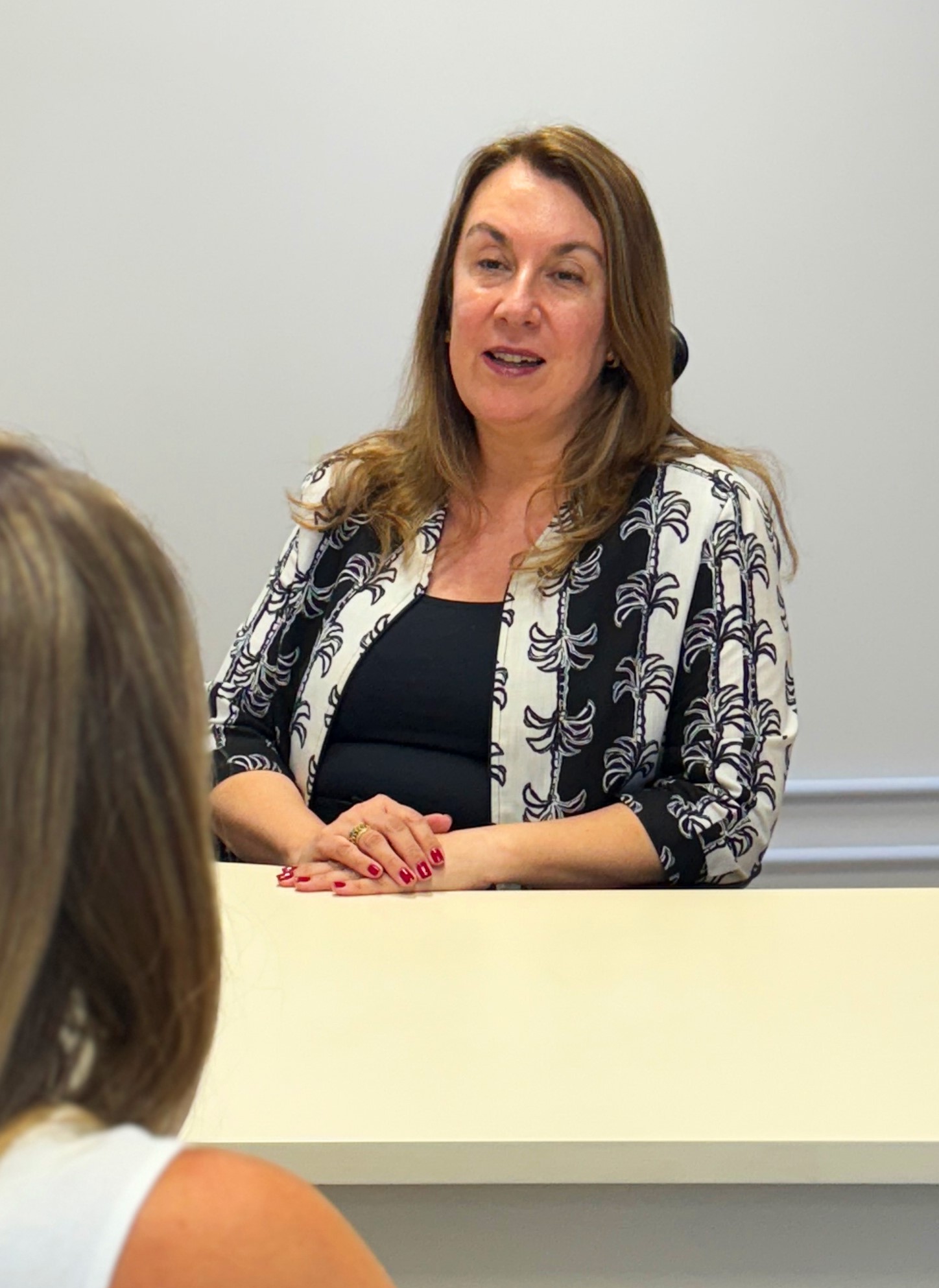 Des. Teresa em sua mesa de trabalho, fala com mulher de costas