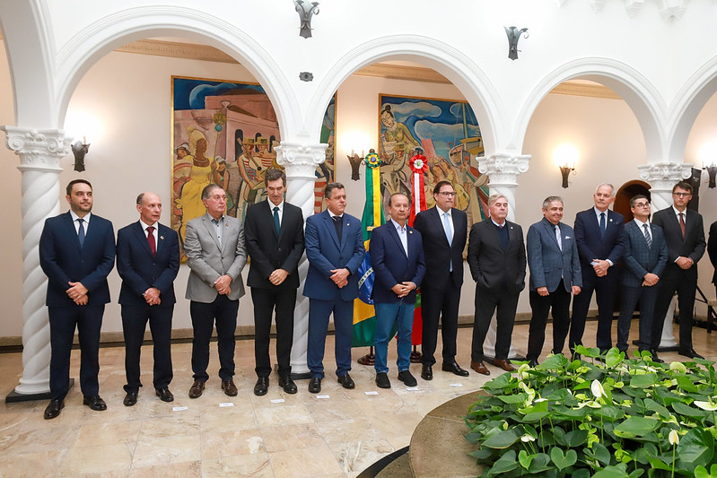 Grupo de homens enfileirados no palácio da agronomica, com obras de arte ao fundo