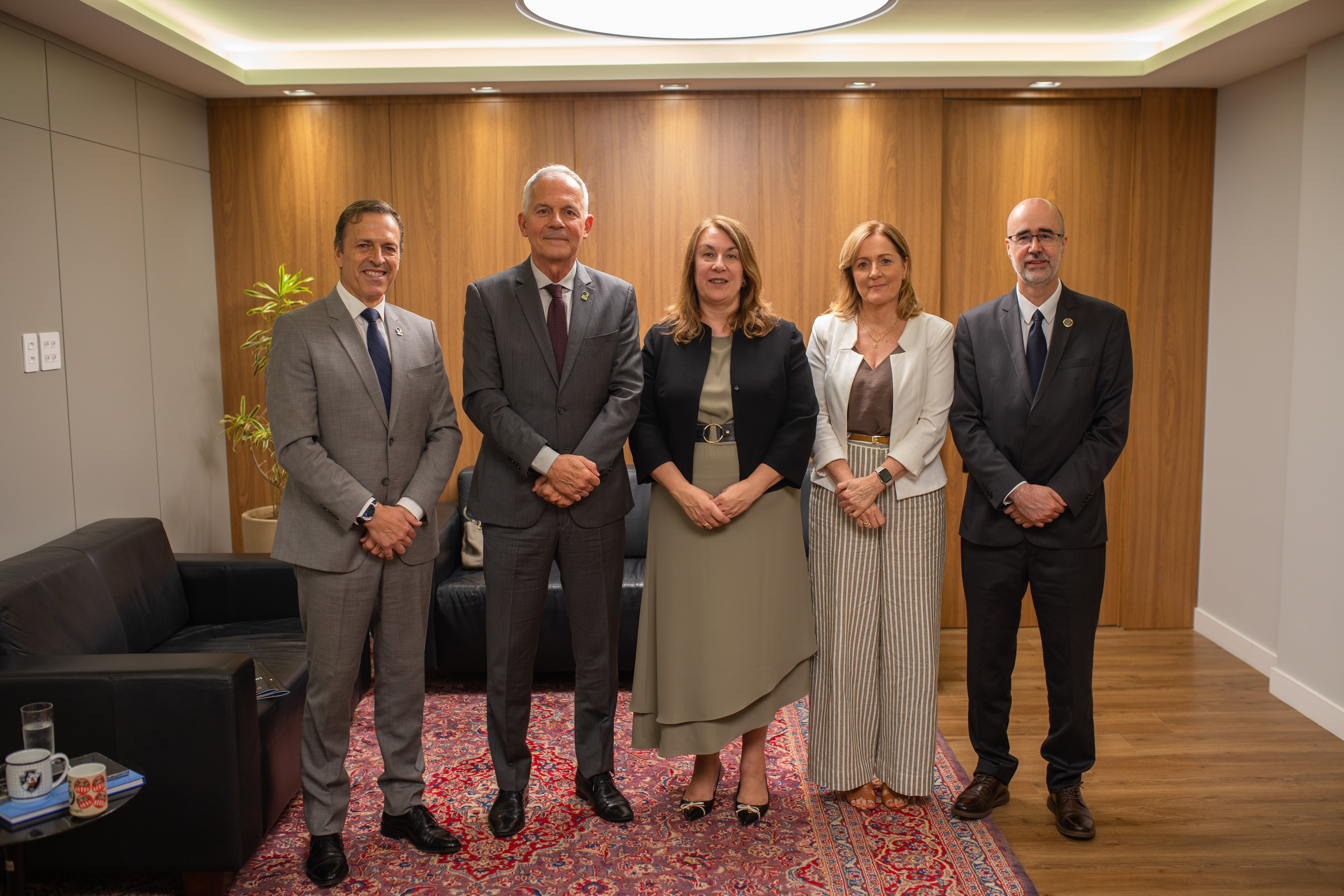 grupo de cinco pessoas posa para foto. ao fundo, um painel de madeira
