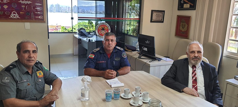 Três homens sentados em uma mesa comprida posam para foto