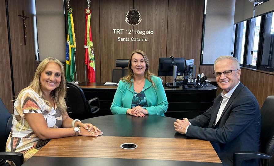 Duas mulheres e um homem sentados à mesa, em formato de U, sorriem