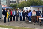 Foto de onze pessoas em um ambiente externo. Atrás de veem carros estacionados, um quiosque e uma van com as portas traseiras abertas, na porta está escrito "MPF"