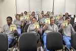 Grupo de pessoas uniformizadas, sentadas em um auditório, segurando duas cartilhas 