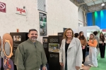 Um homem e uma mulher estão em pé, em uma exposição de fotografia, posando para a foto